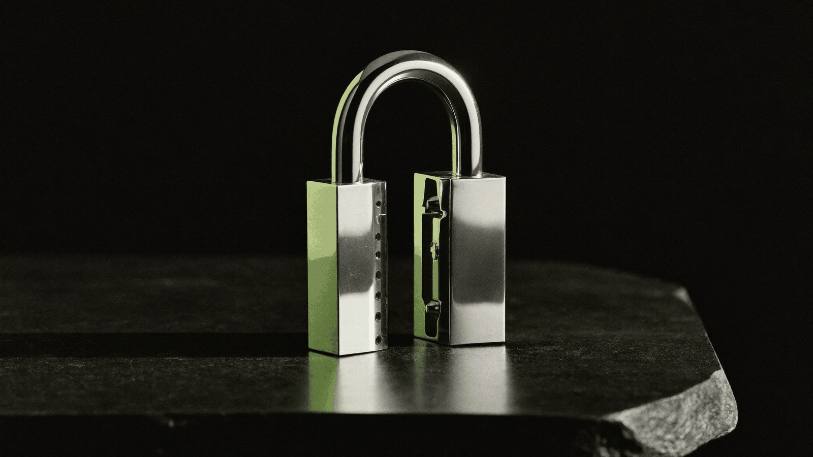 A polished chrome padlock with its shackle open on dark stone