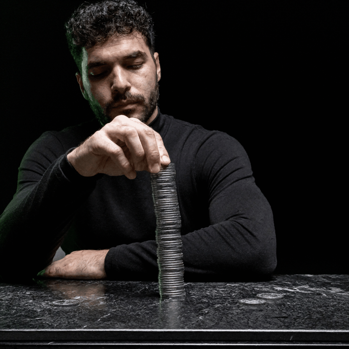 Kassem Kazal stacks plain steel coins into a tall column on a dark stone table