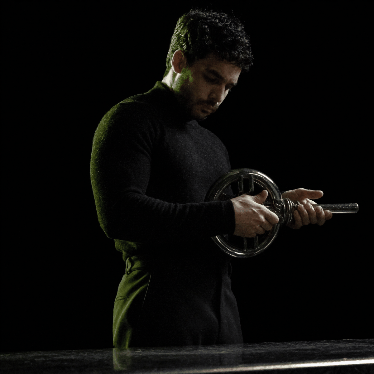 Kassem Kazal holds a polished chrome key in both hands in a dark studio